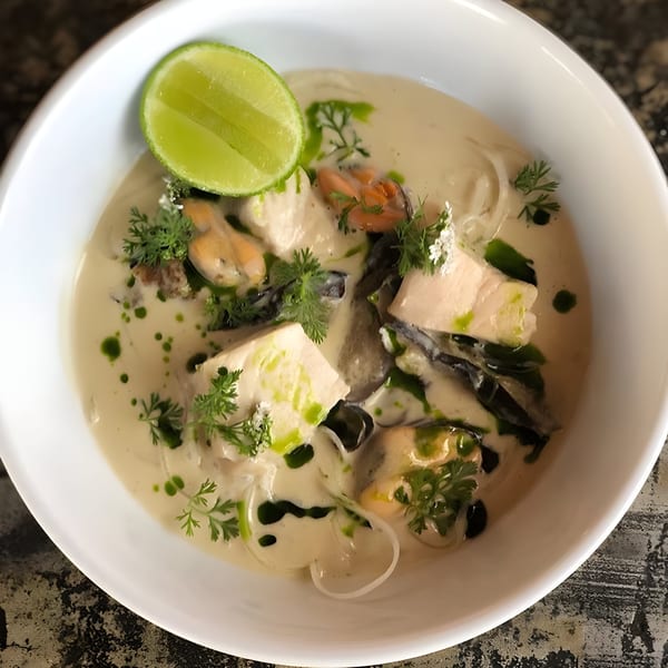 Creamy seafood stew with mussels, fish, herbs, and a lime wedge in a white bowl.