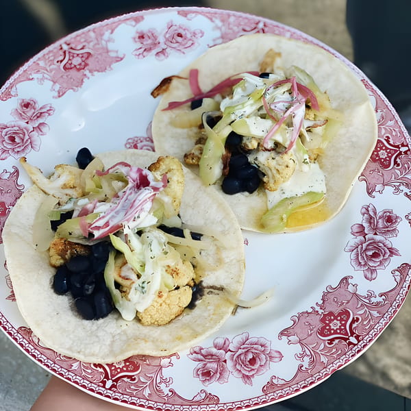 Two cauliflower and black bean tacos with pickled onions and crema on a floral plate.
