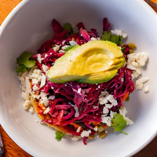 A white bowl filled with a colorful dish of red cabbage, crumbled cheese, and avocado slices.