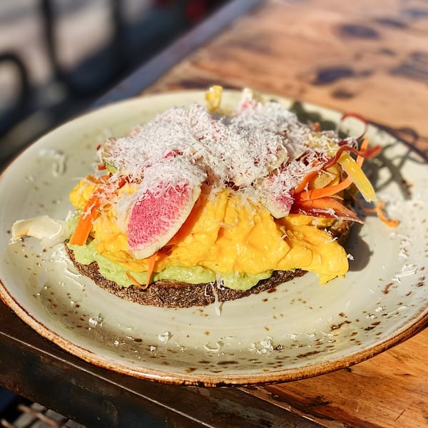 Avocado toast with scrambled eggs, shaved radish, carrots, and shredded cheese on a plate.