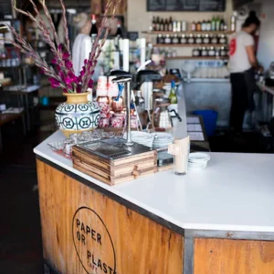 The Paper or Plastik Cafe counter with a vase of purple flowers and a barista working in the background.