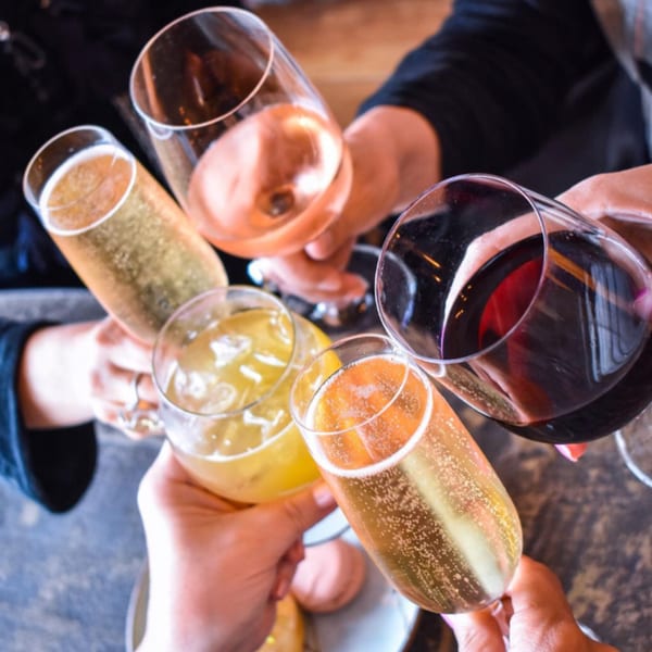 Five hands holding various drinks, including sparkling wine, rosé, red wine, and a yellow cocktail.