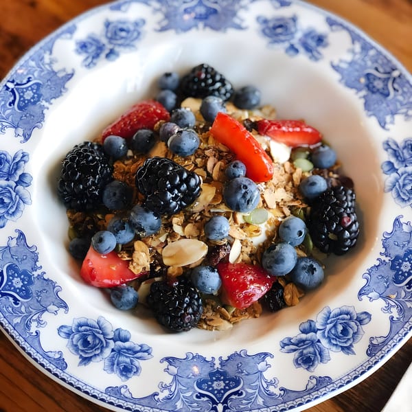 A white bowl with blue floral patterns filled with granola, yogurt, blueberries, blackberries, and strawberries.