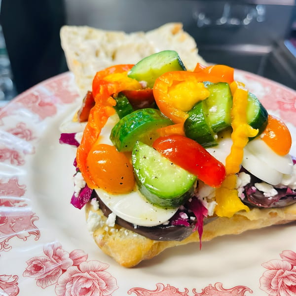 Colorful open-faced sandwich with bell peppers, cucumbers, and feta on a floral plate.