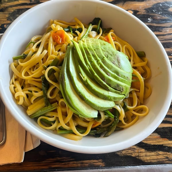 Linguine pasta with asparagus, cherry tomatoes, and sliced avocado in a white bowl.