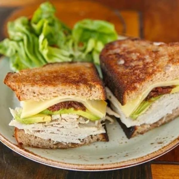 A grilled turkey and avocado sandwich with cheese and sun-dried tomatoes, served with a side salad.
