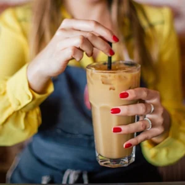 A person in a yellow shirt and blue apron holding an iced coffee with a black straw.