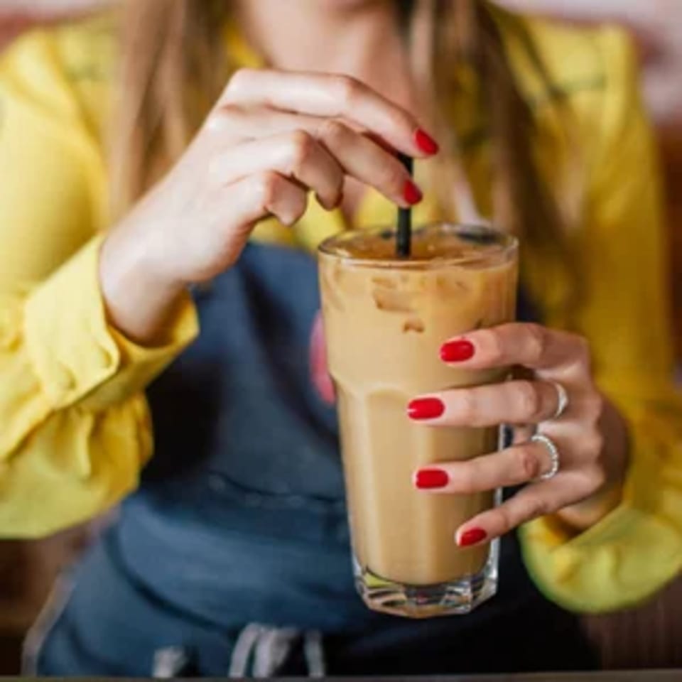 A person in a yellow shirt and blue apron holding an iced coffee with a black straw.