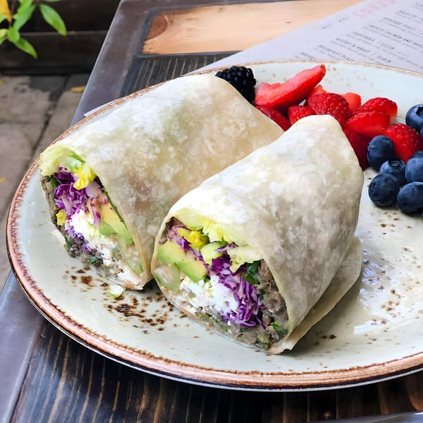 Two breakfast burritos with avocado, cabbage, and feta, served with fresh berries on a plate.