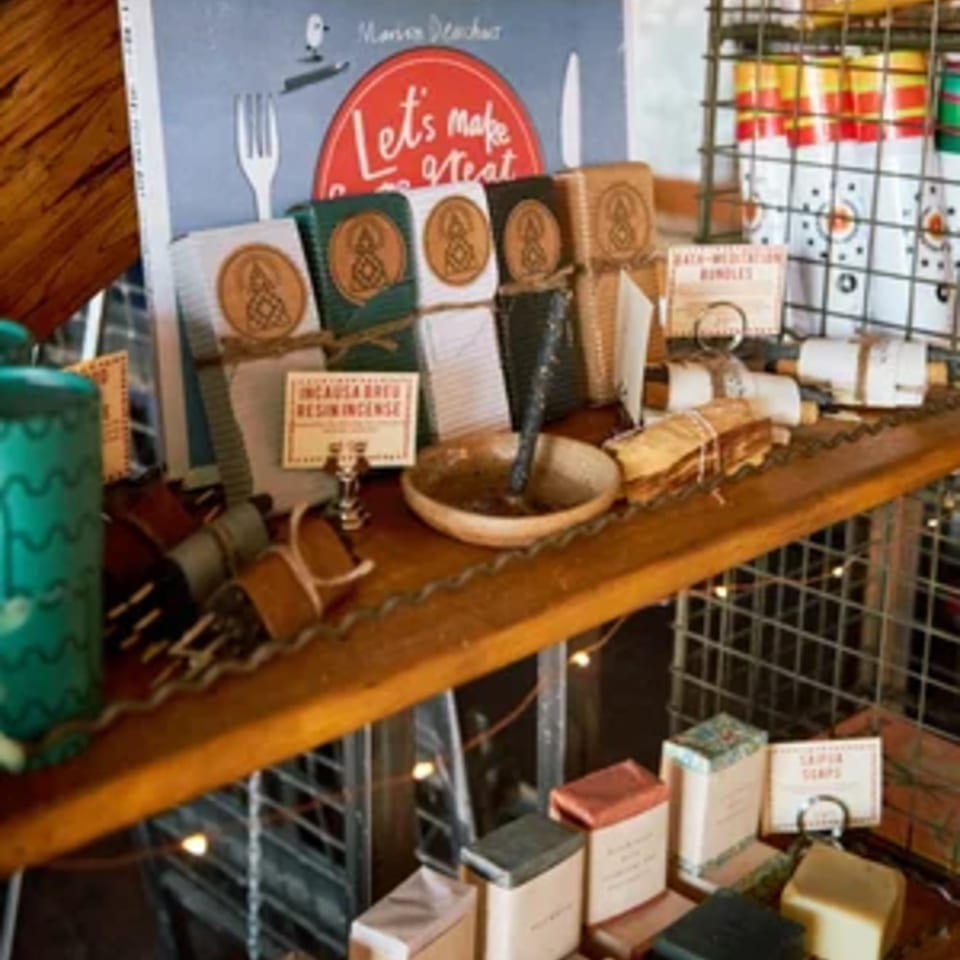 A wooden shelf displays various artisanal items, including incense, soaps, and a cookbook.
